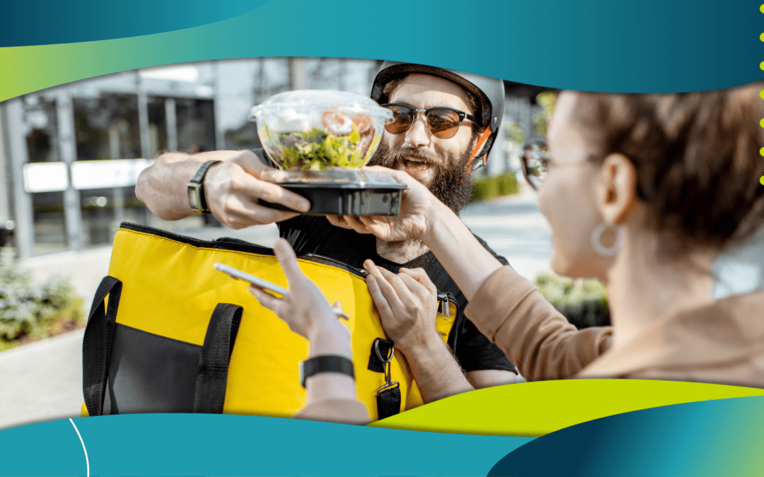 "A man with a yellow delivery bag hands a food container to a woman holding a smartphone, outdoors with buildings in the background.