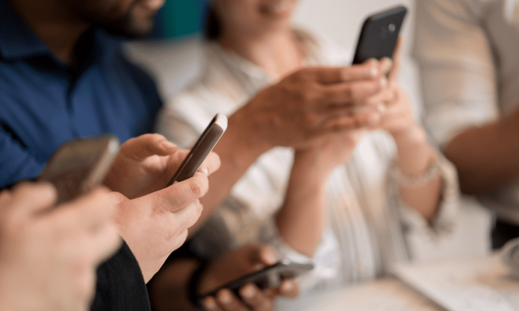 Several women sit in a circle holding their phones as they scroll social media, highlighting the shift in the algorithm that allows small product brands to drive sales through social media ads. 